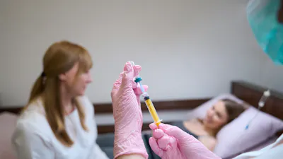 Female doctor communicates with a young patient in a hospital room, next to a nurse preparing an injection