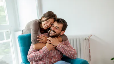 Couple in love sitting in an armchair by the window, hugging and enjoying their time together