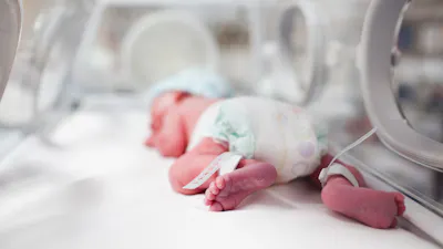 Newborn baby boy covered in vertix inside incubator